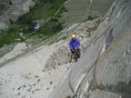 In a warm puffy jacket at the P2 belay, Aspendell in the background; the vansion is parked in the pullout on the road above Colin's head