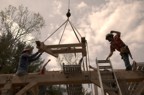 A large subsection of rafters is lifted by crane and positioned around the chimney opening